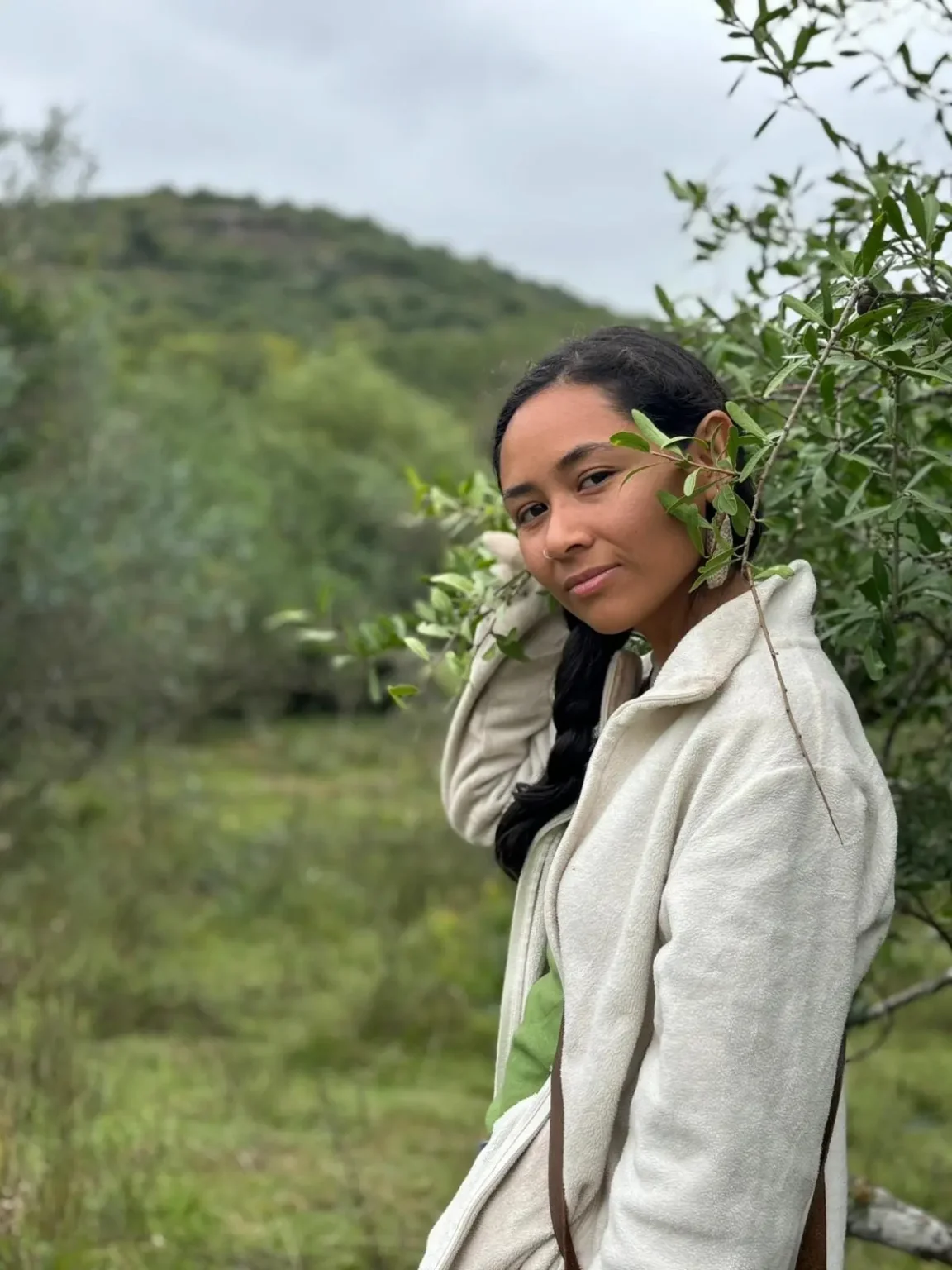 Guidaí Vargas Una Voz Indígena En La Lucha Socioambiental Guidaí Vargas, activista indígena uruguaya, conectada con la naturaleza, con hojas verdes alrededor de su rostro en un entorno natural.