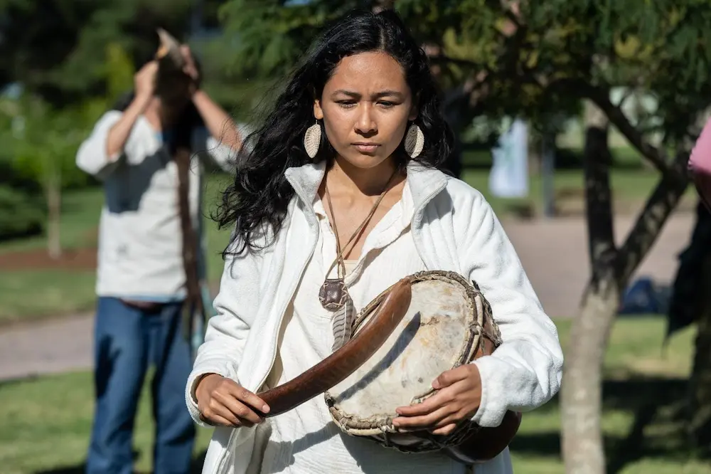 guidai-vargas-ceremonia | Ambienta Guidaí Vargas, activista indígena uruguaya, ejecutando un tambor ancestral en una ceremonia cultural.