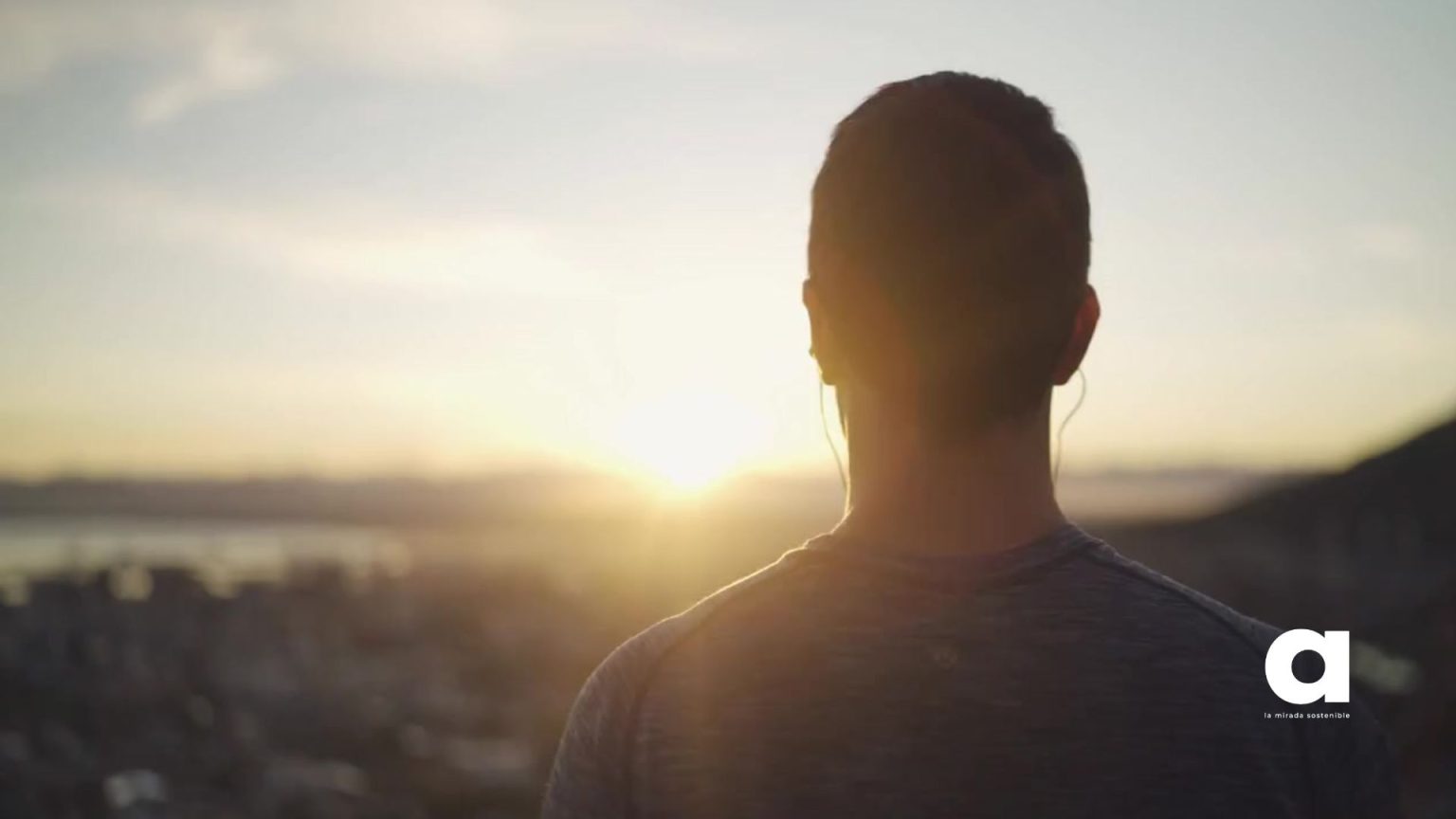 Joven escuchando el podcast Conectados por Naturaleza de Ambienta en auriculares al atardecer en un entorno natural.