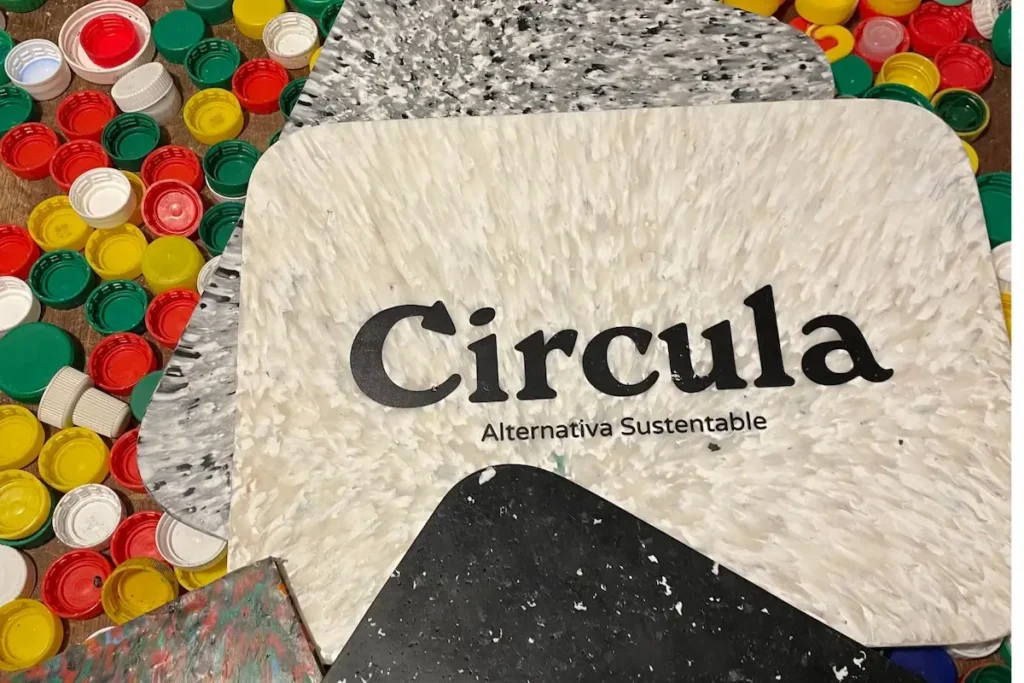 Tapas plásticas de colores junto a placas de material reciclado con el logo de Circula, Alternativa Sustentable.