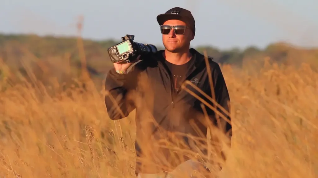 Leandro Borba, fotógrafo de fauna marina en Uruguay, con cámara al hombro entre pastizales costeros.