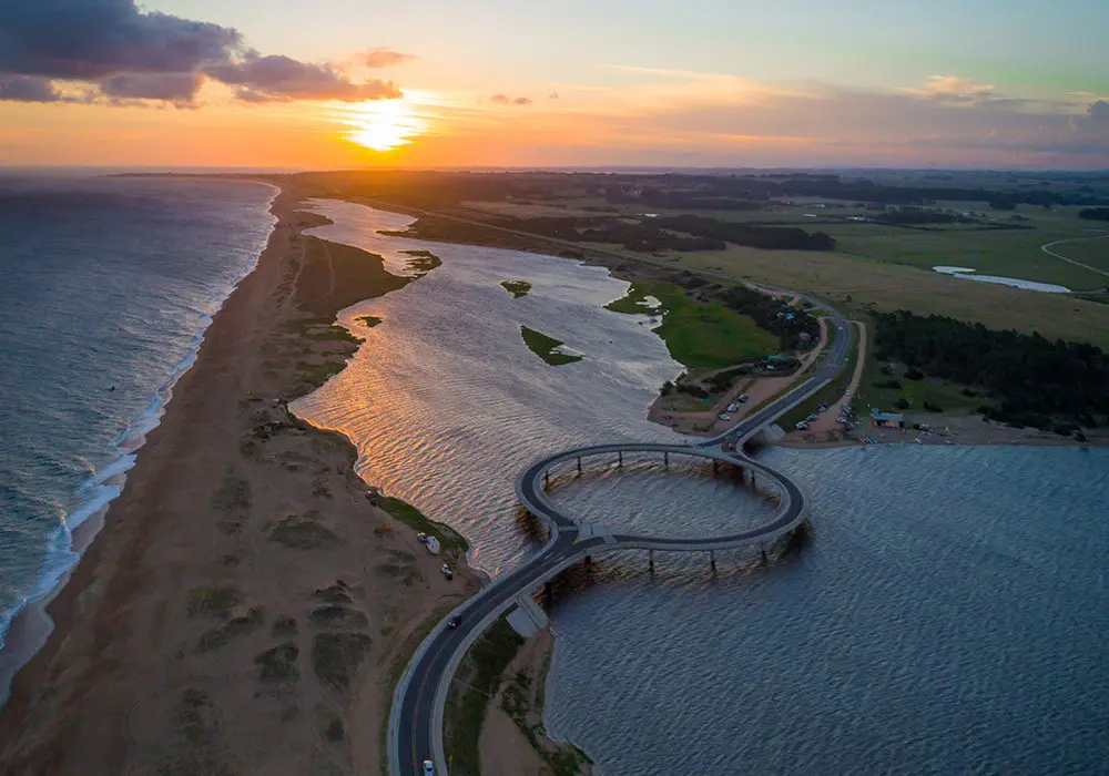Vista aérea del icónico Puente Circular de Laguna Garzón al atardecer, un ecosistema costero protegido por el SNAP Uruguay.