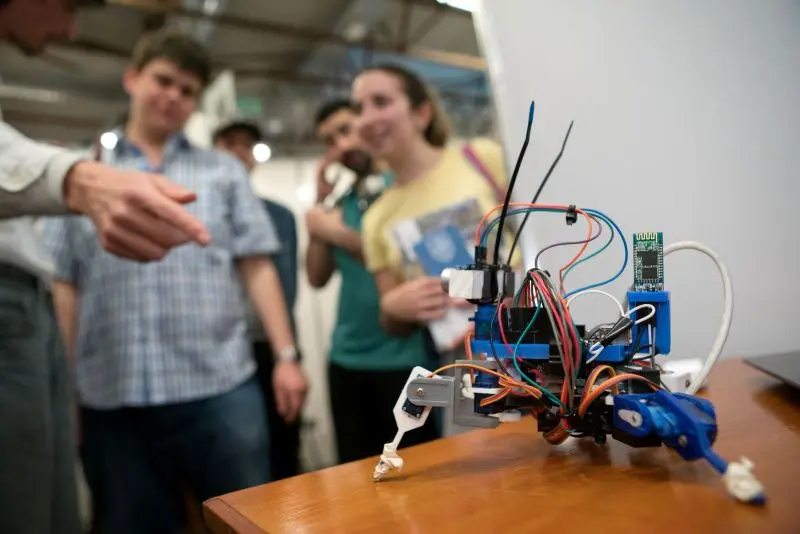 Robot educativo de Ingeniería deMuestra 2025 con jóvenes y docente en stand interactivo.