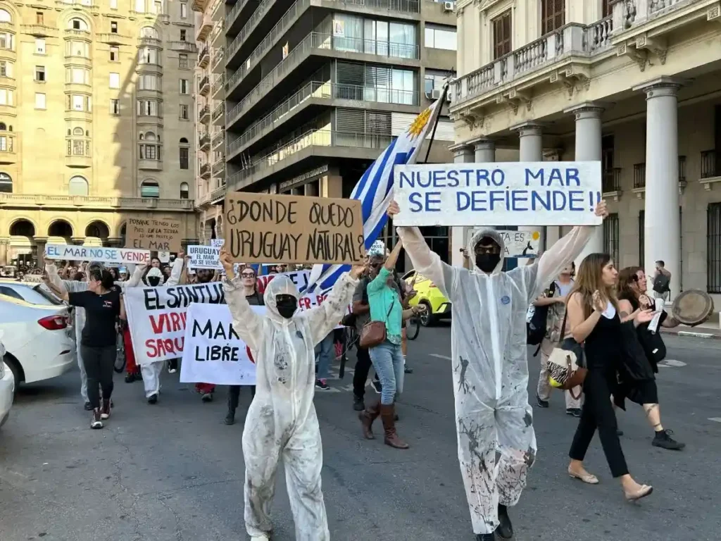 Activistas en mamelucos con manchas de petróleo marchan en Plaza Independencia con carteles en defensa del mar uruguayo.