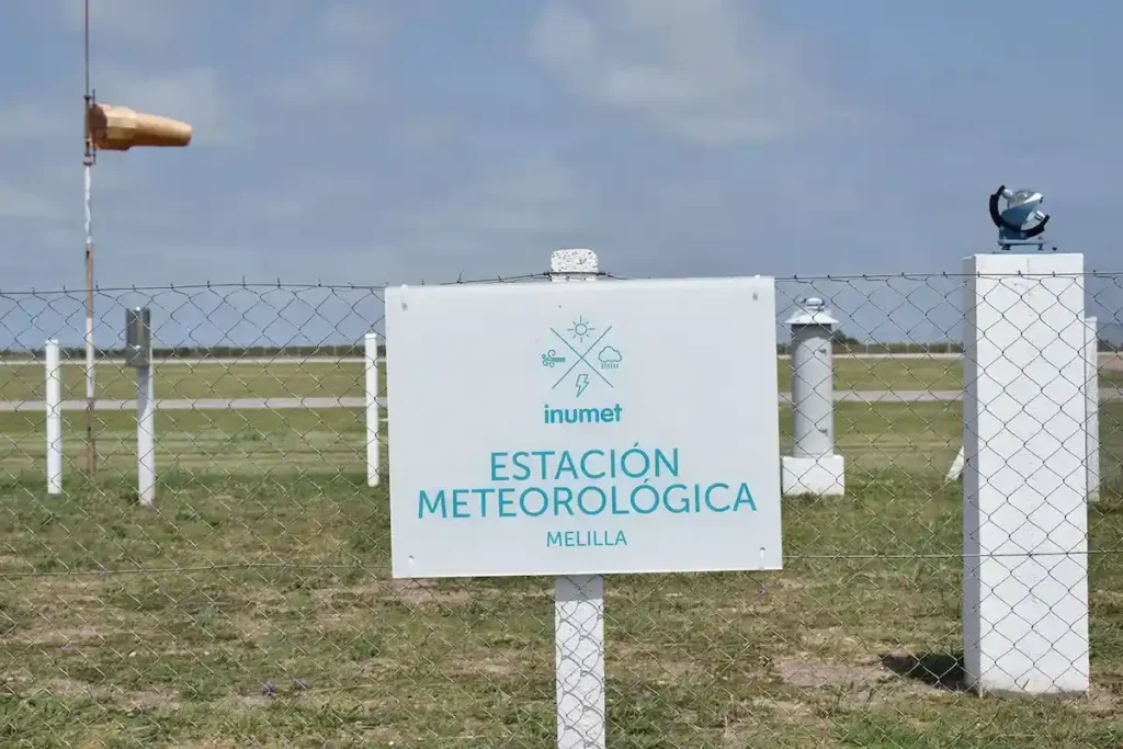 Cartel oficial de la Estación Meteorológica de Melilla de Inumet en Uruguay, con instrumental de medición de variables climáticas de fondo para el monitoreo del fenómeno El Niño en Uruguay.