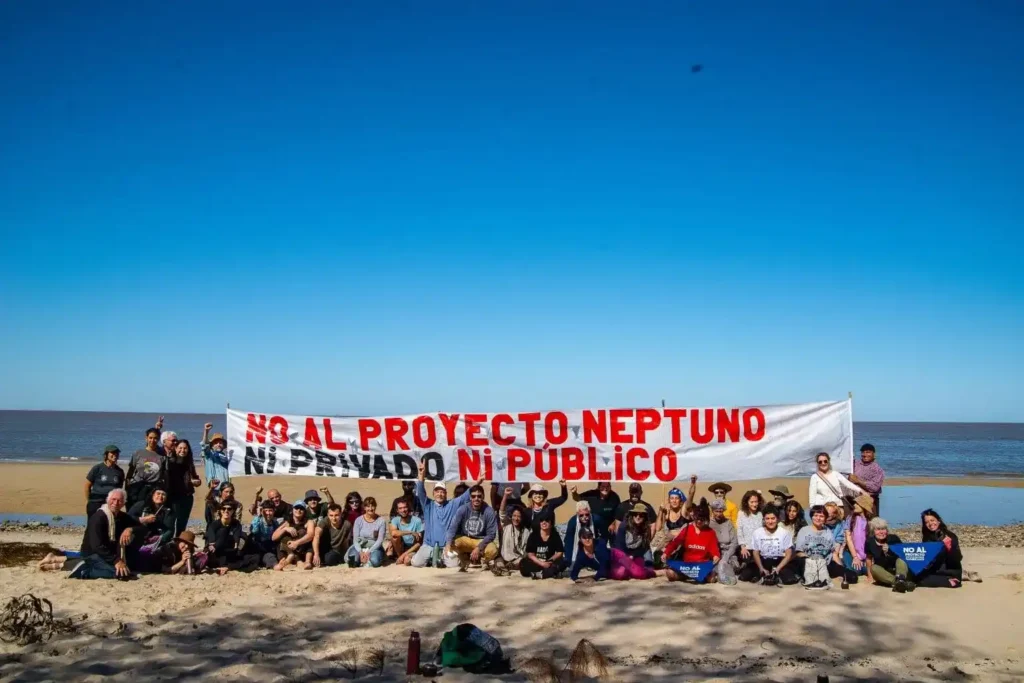Grupo de vecinos y activistas sosteniendo una gran pancarta contra el Proyecto Neptuno en la playa de Arazatí, Uruguay.