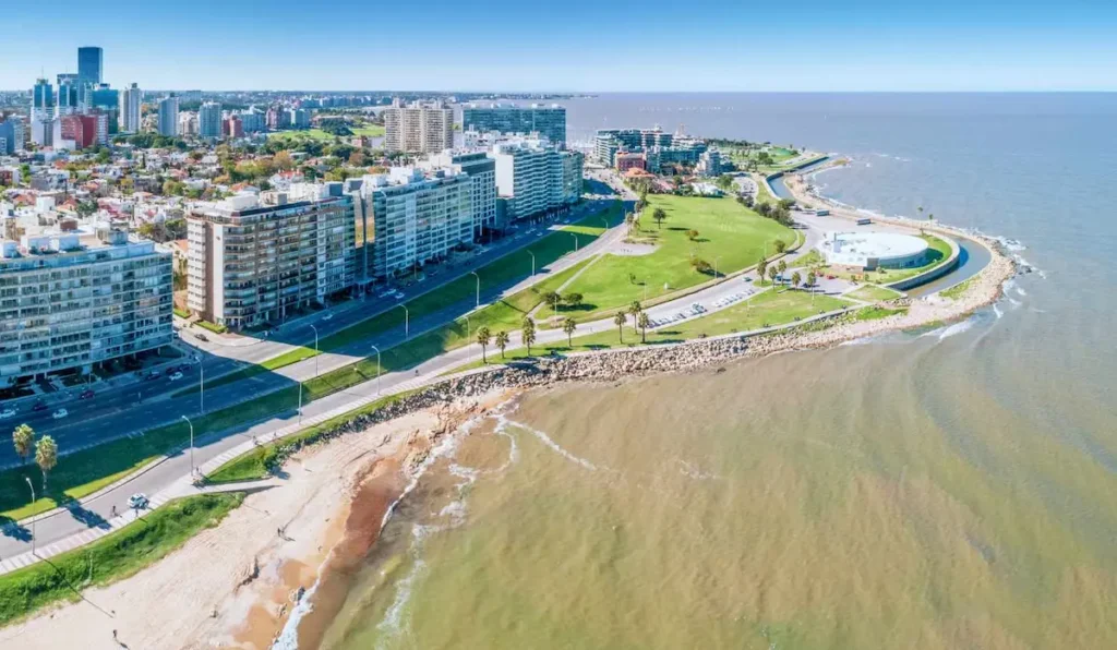 Vista aérea de la rambla y la playa de Pocitos en Montevideo, mostrando el Río de la Plata y la alta densidad de la infraestructura urbana costera.